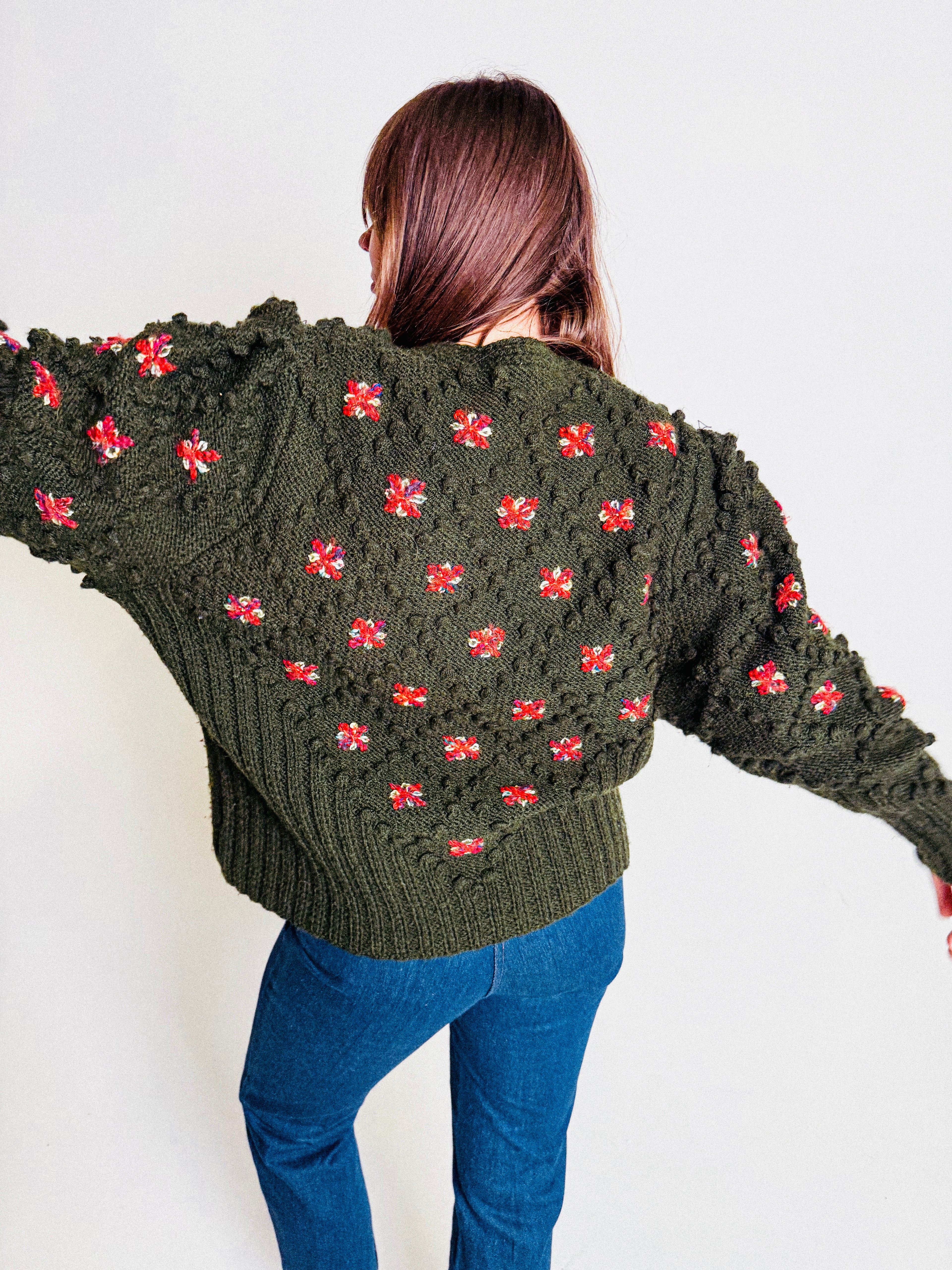 Person wearing a green sweater with red floral patterns on a white background