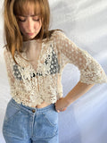 Woman wearing a lace top and jeans against a plain background