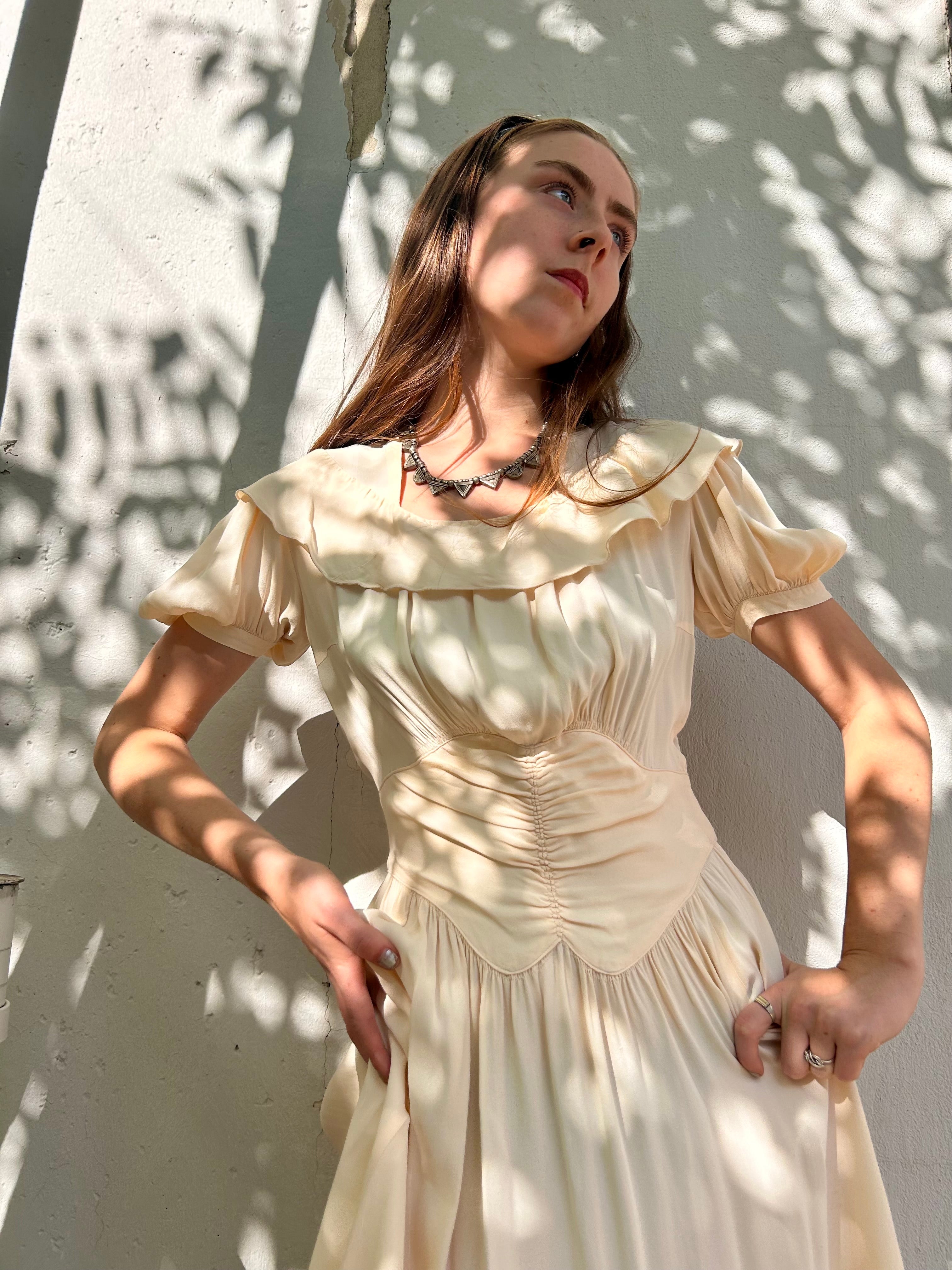 Woman in a vintage-style cream dress standing against a light background