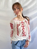 Person wearing a white blouse with red embroidery against a plain background