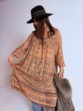 Woman wearing a patterned dress and black hat against a white background