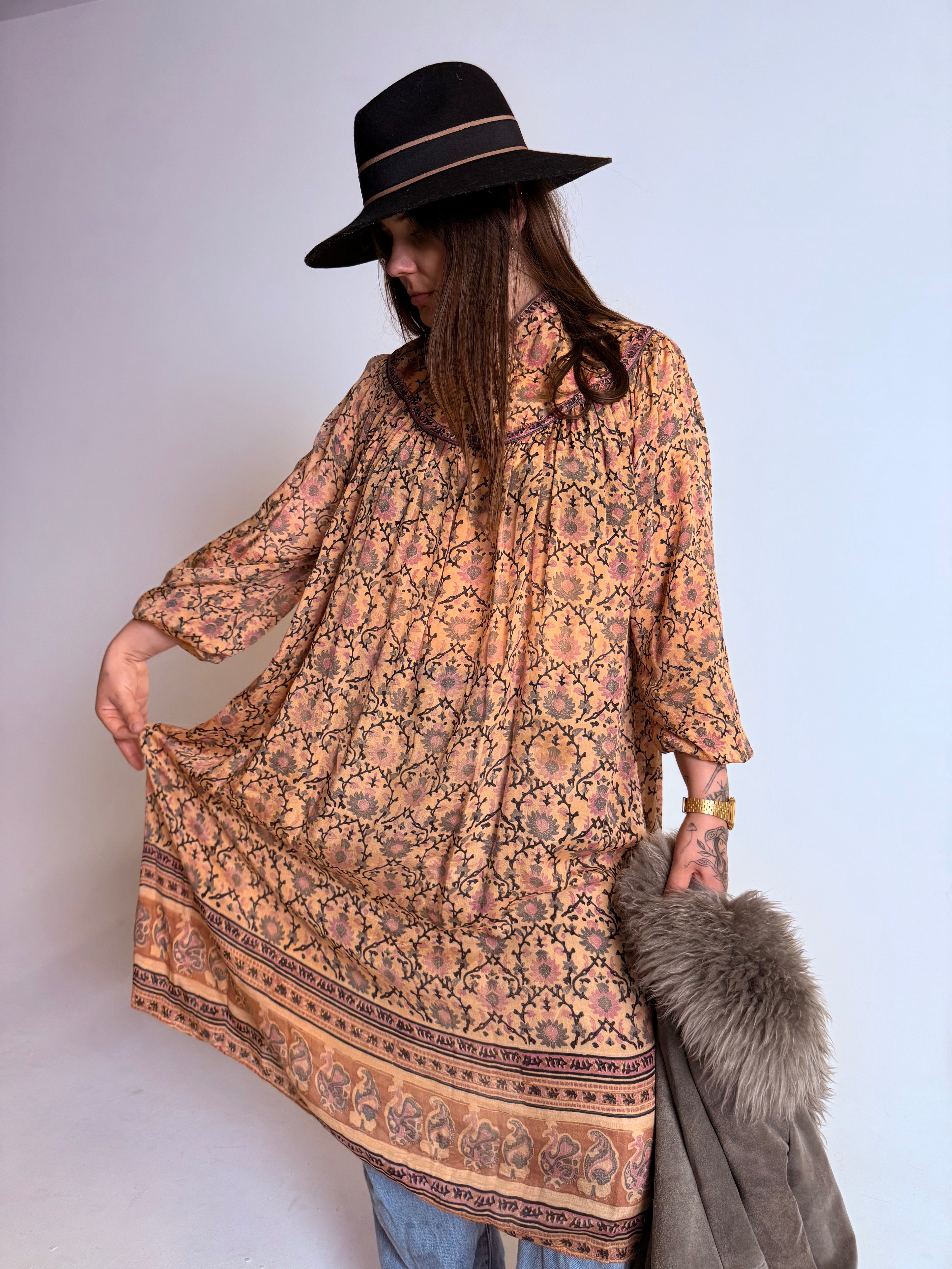 Woman wearing a patterned dress and black hat against a white background