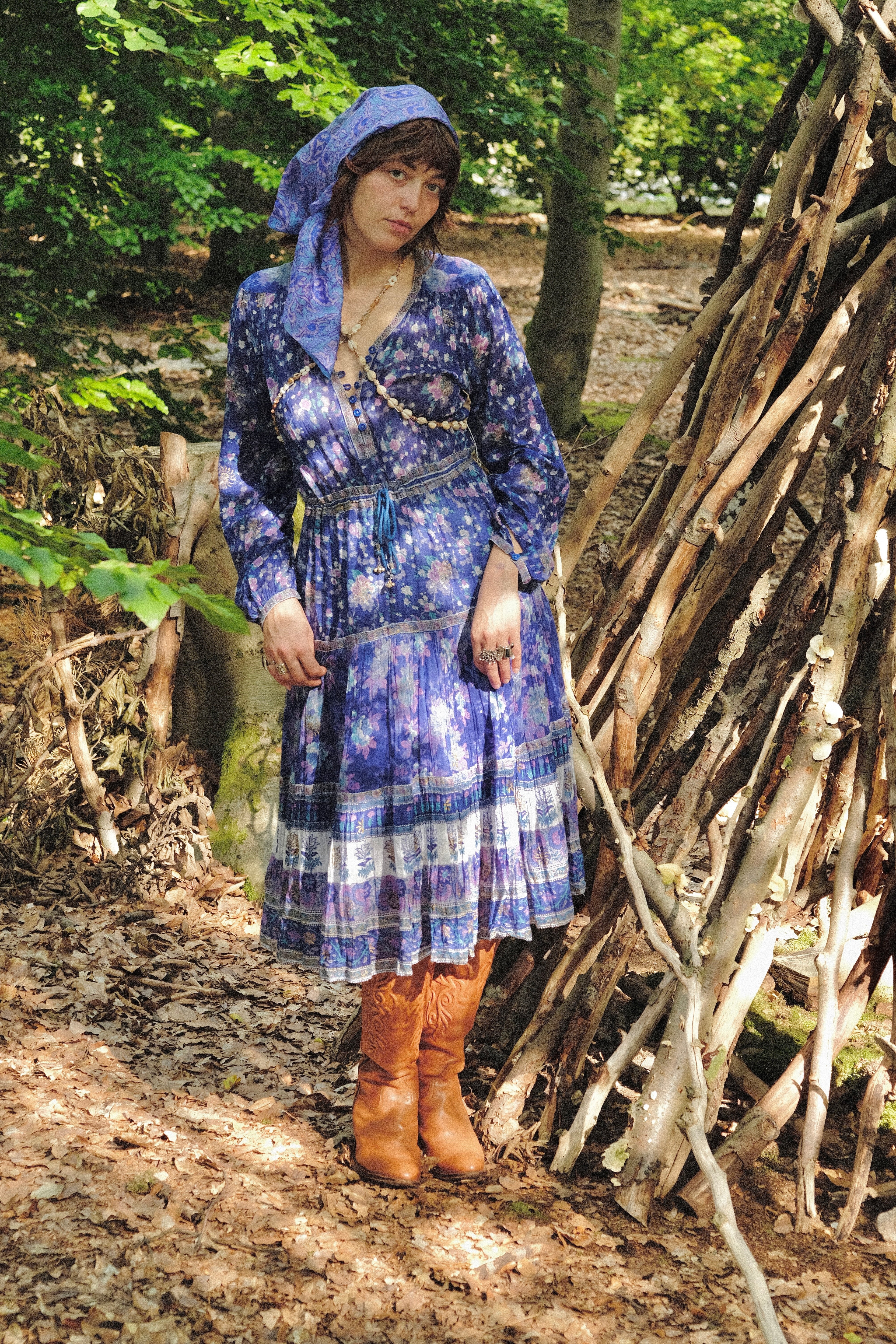 Woman in a blue dress standing near a wooden structure in a forest