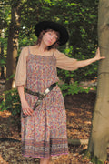 Woman in a floral dress and black hat standing in a forest