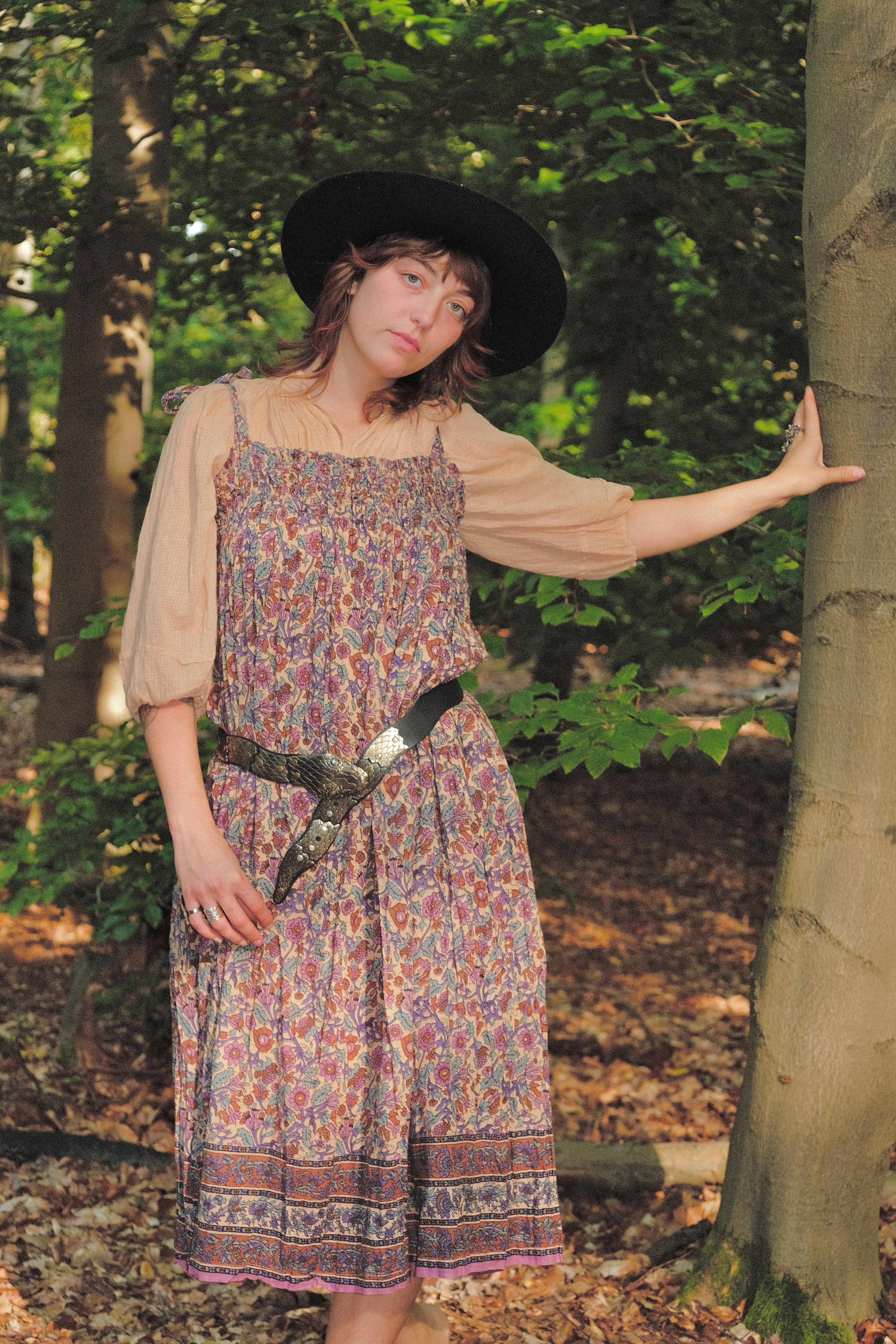 Woman in a floral dress and black hat standing in a forest