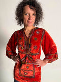 Woman wearing a traditional embroidered orange tunic against a plain background