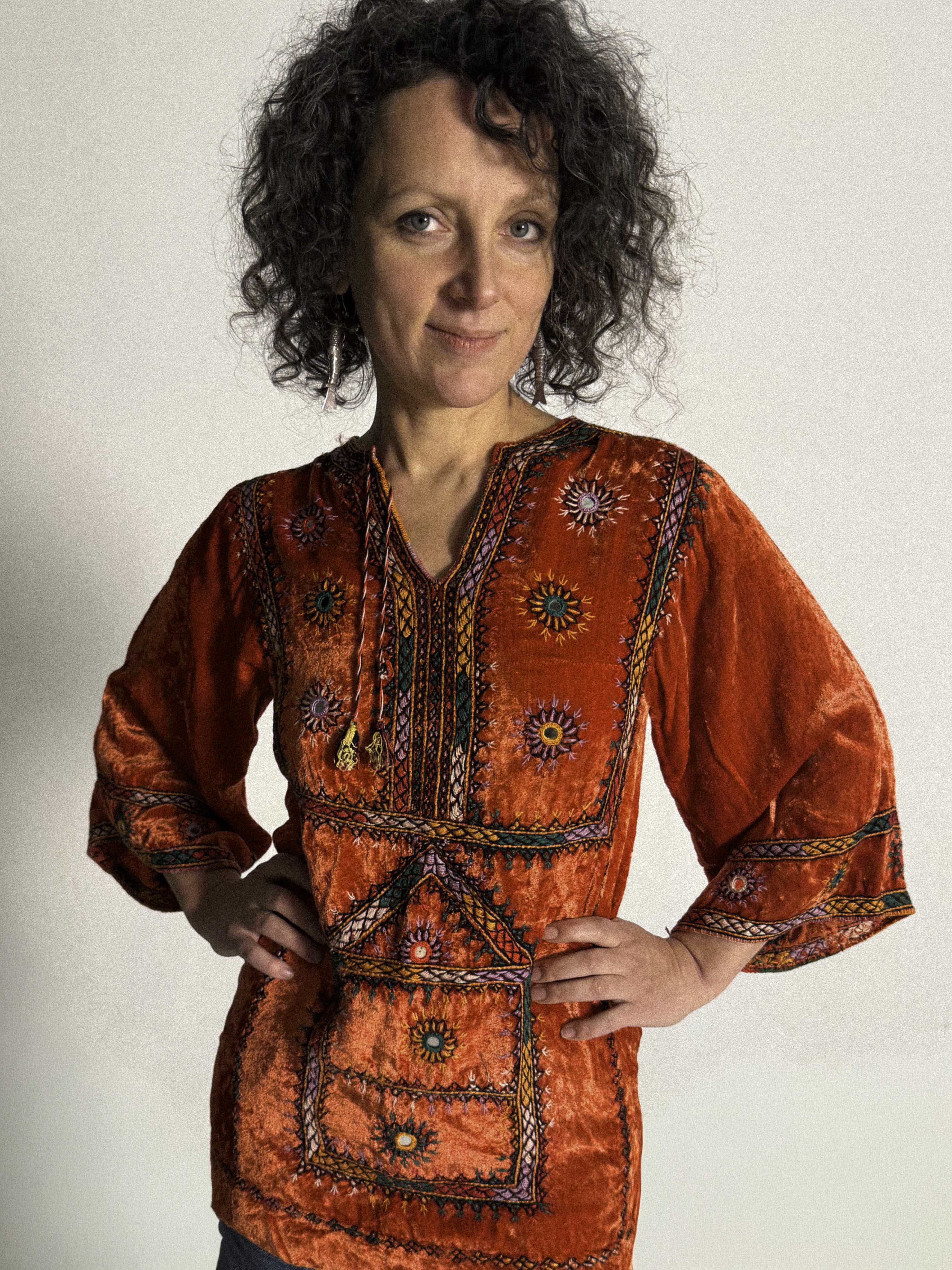 Woman wearing a traditional embroidered orange tunic against a plain background