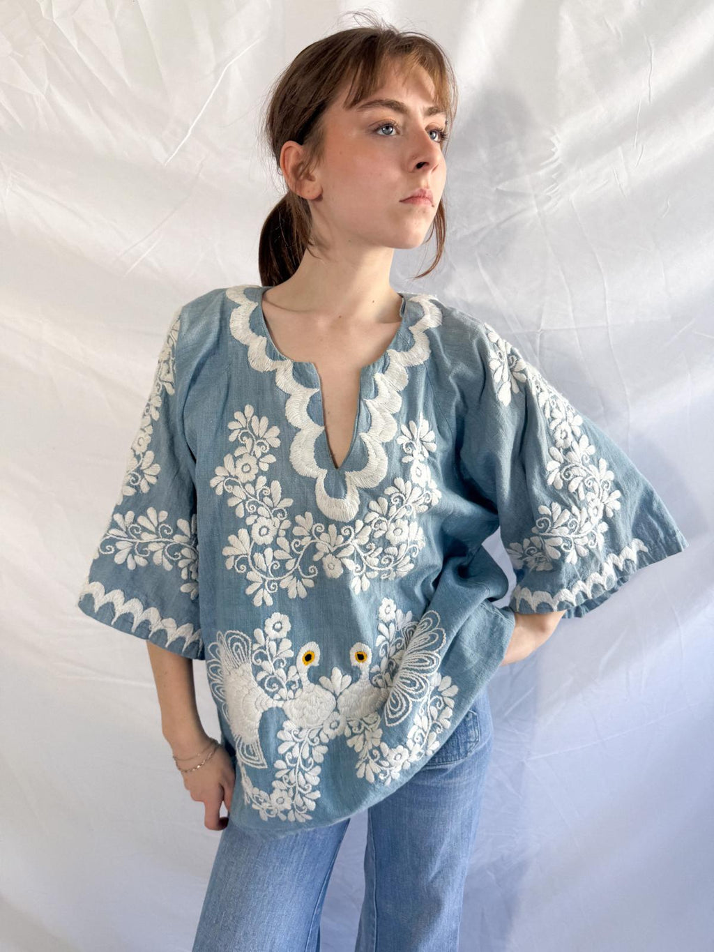 Woman wearing a blue blouse with white floral embroidery against a white background