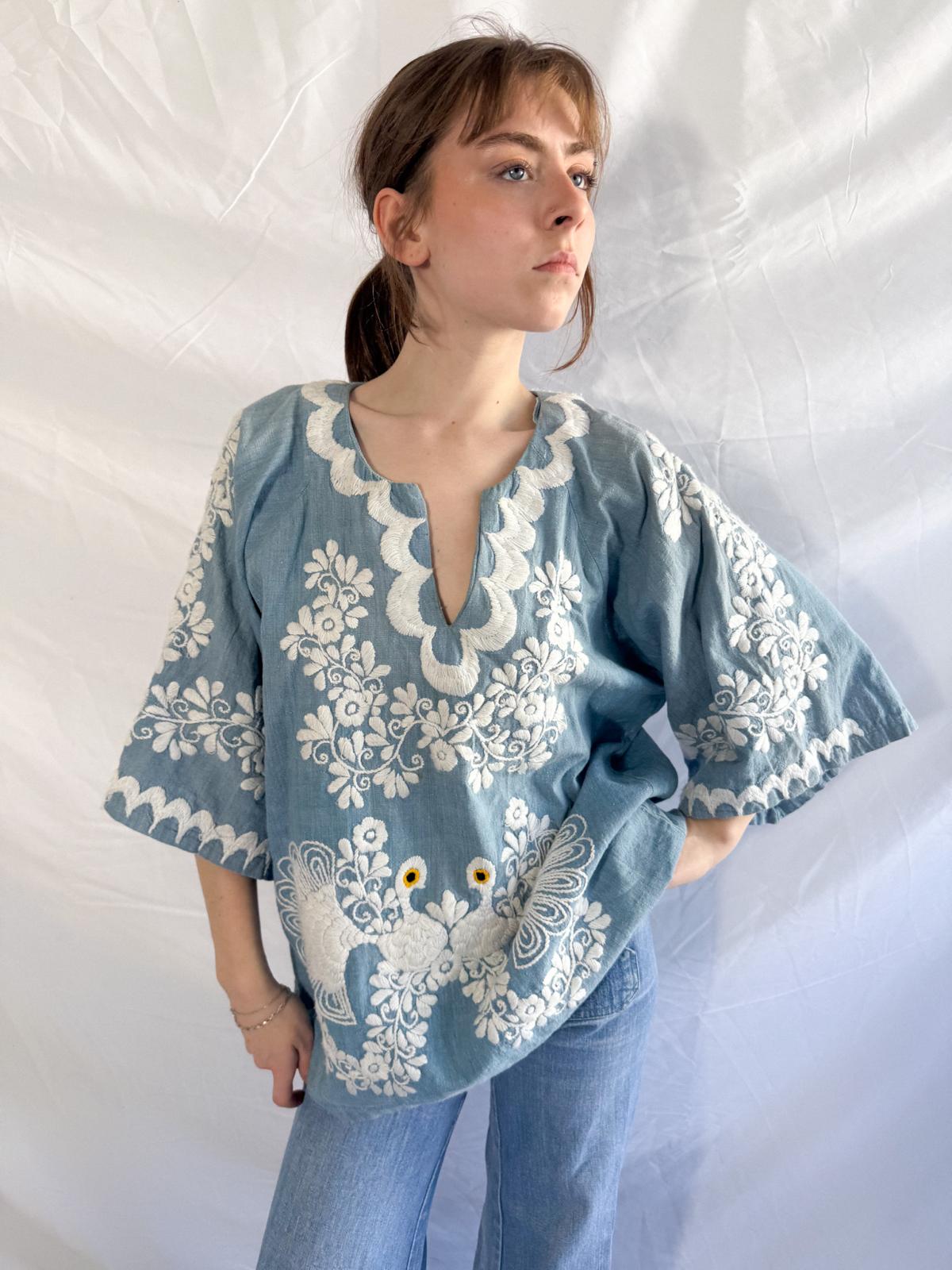 Woman wearing a blue blouse with white floral embroidery against a white background