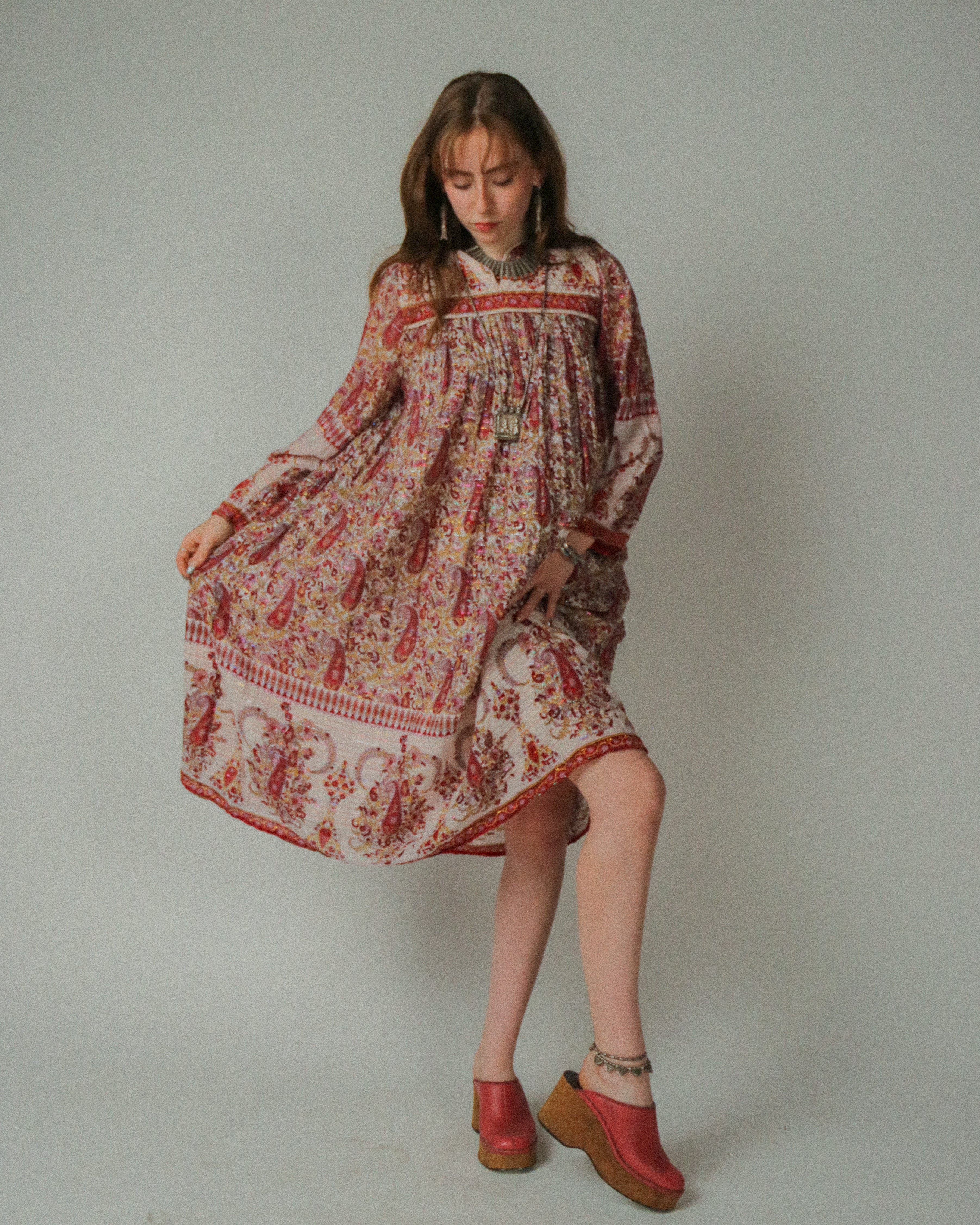 Woman wearing a 1970s Wings Rainbow Lurex Dress  and red shoes on a plain background