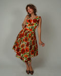 Woman wearing a 1950s Alix of Miami Cocktail Dress with red and orange flowers on a plain background