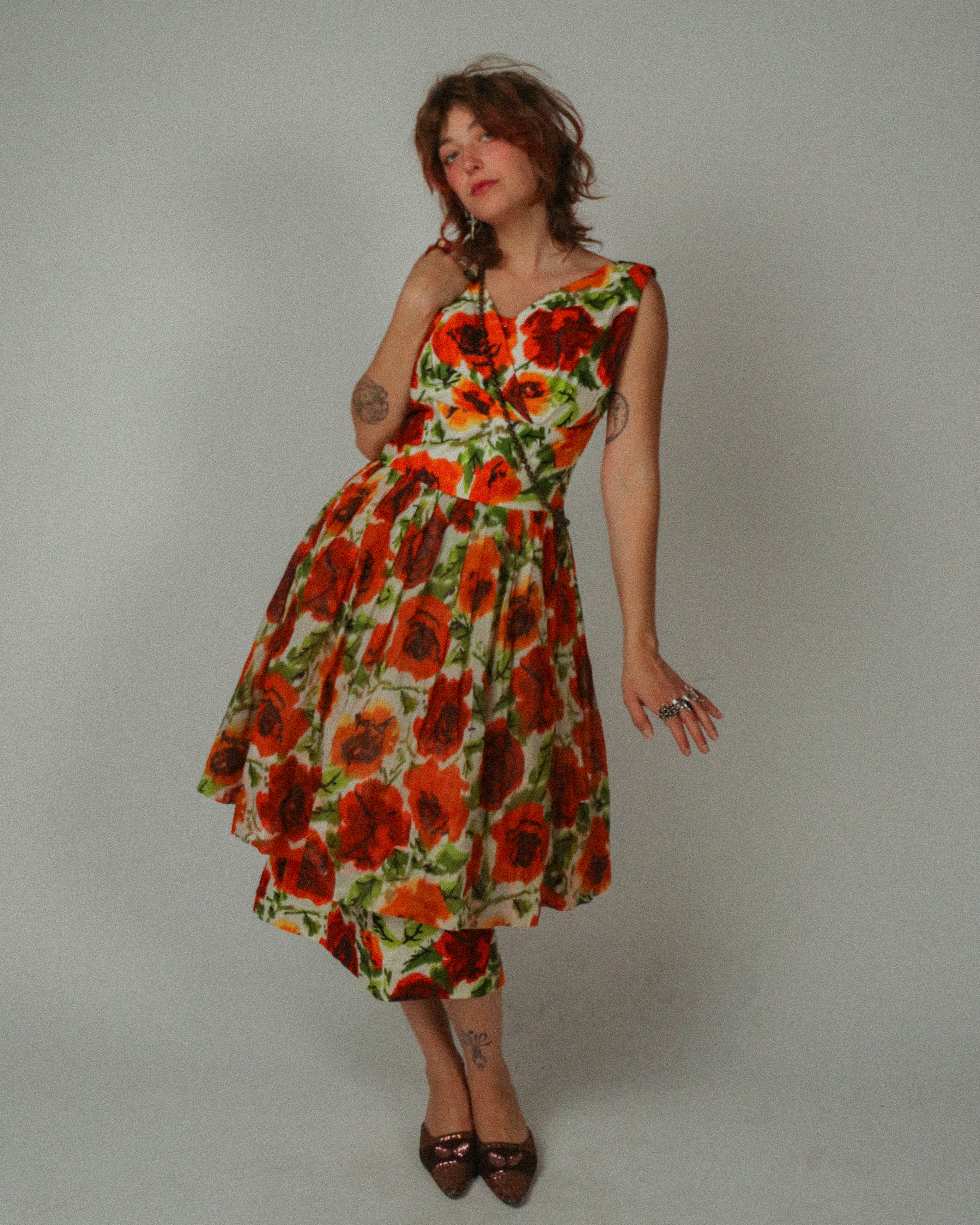 Woman wearing a 1950s Alix of Miami Cocktail Dress with red and orange flowers on a plain background